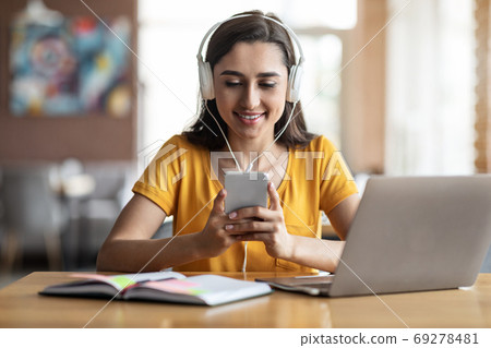 Young girl student sitting at cafe, using laptop and smartphone Young girl student sitting at cafe, using laptop and smartphone 69278481