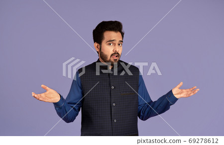 Who knows. Confused Indian guy shrugging shoulders on violet background Who knows. Confused Indian guy shrugging shoulders on violet background 69278612