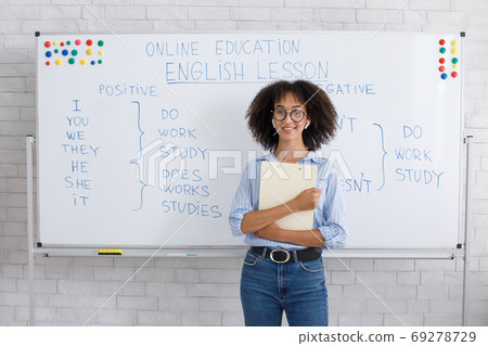 Cute african american girl in wireless headphones and glasses holding notepad on whiteboard background 69278729