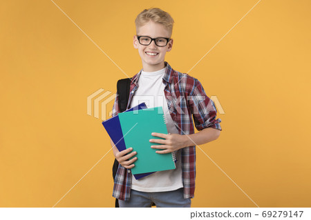 Smiling guy holding textbooks at orange studio background Smiling guy holding textbooks at orange studio background 69279147
