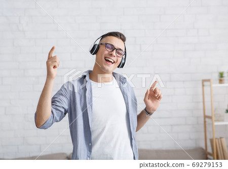 Free time and joy at home. Happy guy in headphones and glasses dancing and singing 69279153