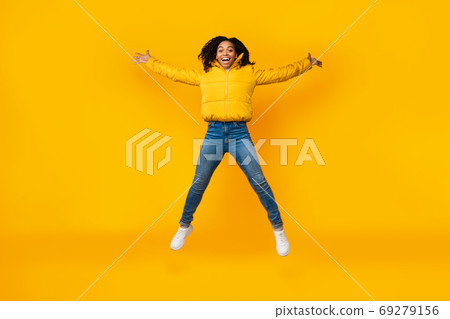 Joyful African Girl Doing Spread Eagle Jump Over Yellow Background Joyful African Girl Doing Spread Eagle Jump Over Yellow Background 69279156