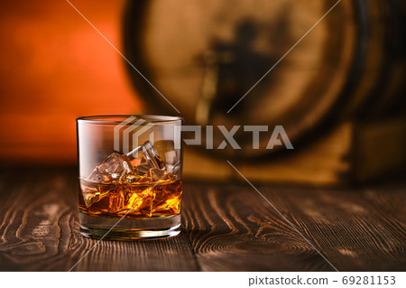 Glass of whiskey with ice with barrel on background 69281153
