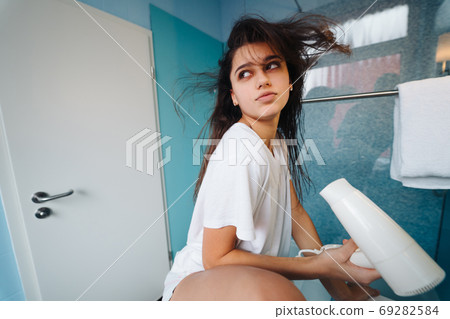 Portrait of young woman using hairdryer in bathroom 69282584