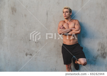 Natural portrait of young athletic shirtless man standing near concrete wall. Natural portrait of young athletic shirtless man standing near concrete wall. 69282944