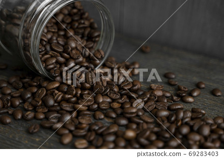 Roasted fresh arabica coffee beans scattered on a table from a little jar on a wooden table. Fresh coffee beans. 69283403