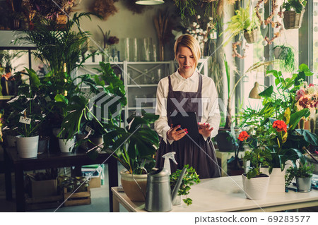 Entrepreneur Makes Notes On Her Tablet in Cosy Greenhouse. Entrepreneur Makes Notes On Her Tablet in Cosy Greenhouse. 69283577