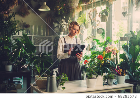 Focused Florist Writes Message From Tablet in Greenhouse. Focused Florist Writes Message From Tablet in Greenhouse. 69283578