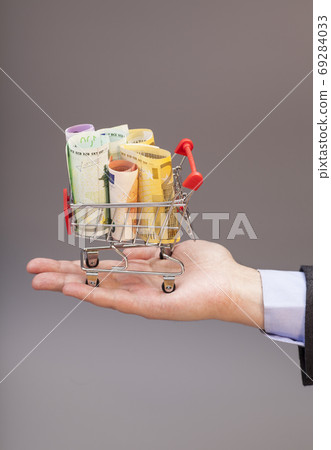 Shopping cart with euro banknotes on hand isolated on gray 69284033
