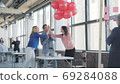 A young woman manager walks in the office with red balloons and congratulates a colleague. Happy birthday to colleagues. Coworking. Modern trendy office interior in a loft style 69284088