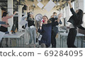Colleagues perform a hand dance in the office during a break. A man rolls an employee in a chair, colleagues join in, scatter money, dance and shout into a megaphone. Fun athmosphere. 69284095