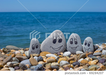 Group of stones with drawn faces in the sand. Father, mother, daughter and son. Concept of happy family. Group of stones with drawn faces in the sand. Father, mother, daughter and son. Concept of happy family. 69284207