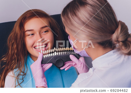 The dentist comparing patient's teeth shade with samples for bleaching treatment. 69284482