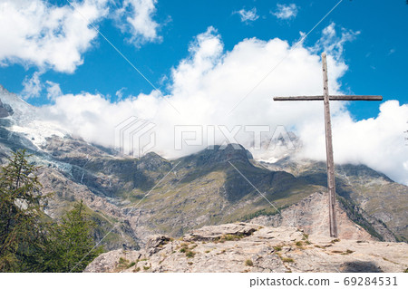 Alpine Cross. An alpine landscape containing a large wooden cross. Beautiful mountain landscape in Austria with blue sky Alpine Cross. An alpine landscape containing a large wooden cross. Beautiful mountain landscape in Austria with blue sky 69284531