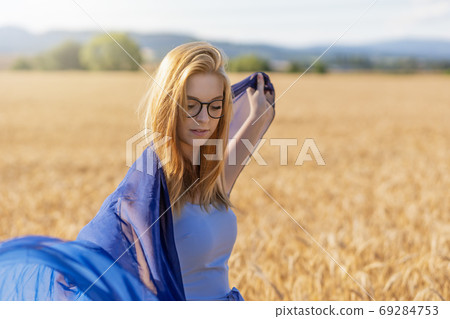 Cool young woman is playing with a blue scarf in corn field. 69284753