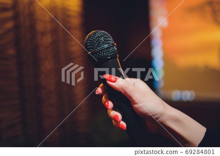 Microphone and female singer close up. Woman singing into a microphone, holding mic with hands. Microphone and female singer close up. Woman singing into a microphone, holding mic with hands. 69284801