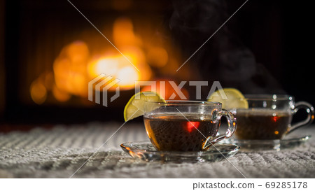 Two cups of tea with lemon on the background of the fireplace. Stand on a white knitted tablecloth 69285178