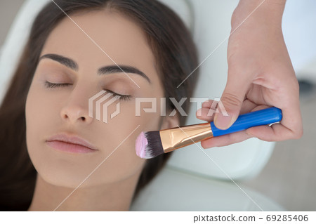 Cosmetologist applying facial mask on her customers face Cosmetologist applying facial mask on her customers face 69285406