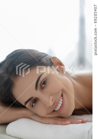 Dark-haired woman lying down after beauty procedures and smiling 69285407