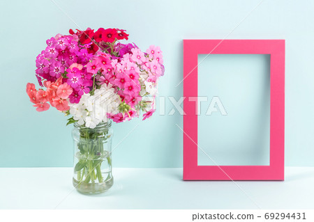 Bouquet of bright colored flowers in vase and wooden empty frame on table against the background of blue wall. Template for greeting card, invitation. Mockup Copy space Front view Bouquet of bright colored flowers in vase and wooden empty frame on table against the background of blue wall. Template for greeting card, invitation. Mockup Copy space Front view 69294431