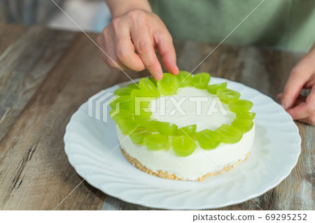 A woman's hands making a Shine Muscat rare cheesecake decoration 69295252