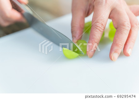 一位女士正在切開閃亮麝香葡萄來裝飾一塊罕見的起司蛋糕 一位女士正在切開閃亮麝香葡萄來裝飾一塊罕見的起司蛋糕 69295474