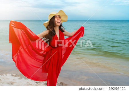 woman with arms spread in a red dress on the sea beach with wind 69296421