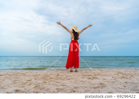 freedom woman in a red dress with arms raised on sea beach 69296422