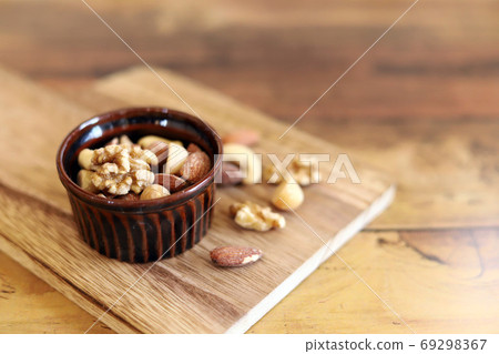 Mixed nuts, brown cocotte and wooden cutting board 69298367