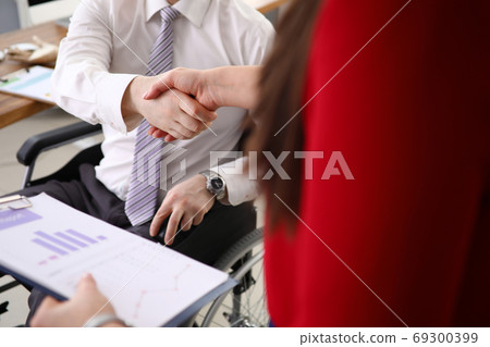 In office, man in wheelchair greets a colleague with handshake. In office, man in wheelchair greets a colleague with handshake. 69300399