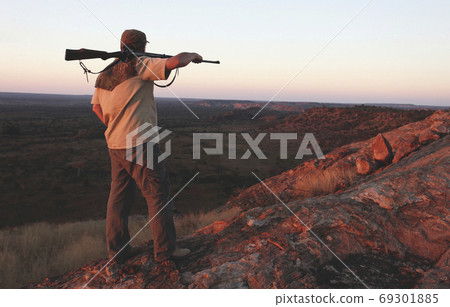 Hunter with  rifle on his shoulder looking down the mountain 69301885