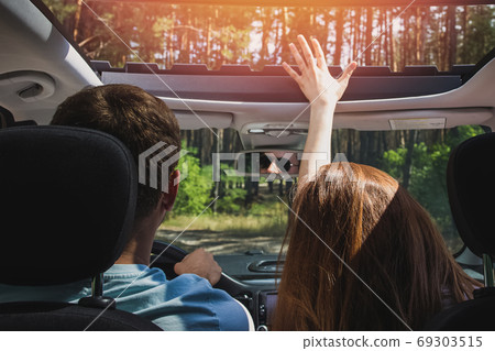 Couple in the car travelling outside the city on the road through trees. Couple in the car travelling outside the city on the road through trees. 69303515