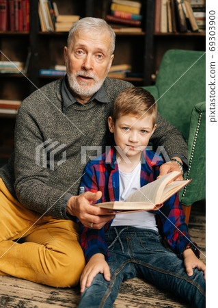 Portrait of happy child boy sitting with his grandfather and reading an interesting book 69303900