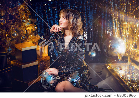 Young beautiful woman in elegant evening dress sitting on floor near christmas tree and presents on a new year eve. Interior with christmas decorations. Shallow DOF and bokeh background Young beautiful woman in elegant evening dress sitting on floor near christmas tree and presents on a new year eve. Interior with christmas decorations. Shallow DOF and bokeh background 69303960