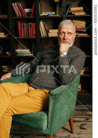 Portrait of thinking bearded gray-haired mature male , thoughtfully holding fist hand near chin. 69303991