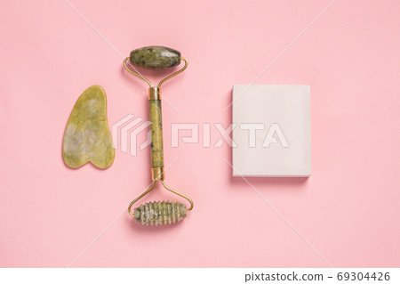Guasha green natural gemstone face roller on pink background. Anti aging self care tool. Guasha green natural gemstone face roller on pink background. Anti aging self care tool. 69304426