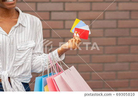 Discount, bonuses and cashback from stores. African american girl with bags holds credit and discount cards in hand Discount, bonuses and cashback from stores. African american girl with bags holds credit and discount cards in hand 69305810