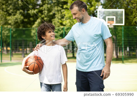 Mature dad embracing little boy who holding basket ball 69305990