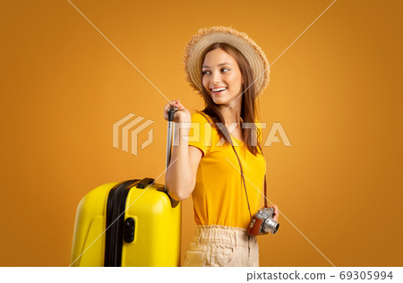Smiling woman traveller with camera carrying suitcase Smiling woman traveller with camera carrying suitcase 69305994