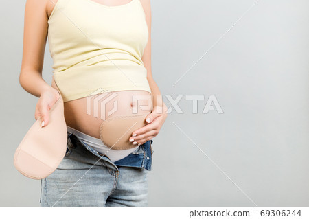 Cropped image of young pregnant woman dressing pregnancy bandage 69306244