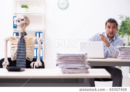 Young male employee and skeleton in the office Young male employee and skeleton in the office 69307408