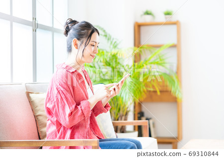 一個女人在沙發上放鬆的同時操作智能手機。 69310844