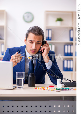 Young male employee and a lot of pills on the desk 69311489