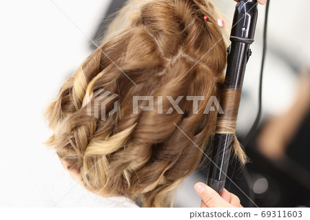 Hairdresser makes curls on women's hair with curling iron Hairdresser makes curls on women's hair with curling iron 69311603
