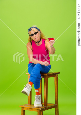 Senior woman in ultra trendy attire isolated on bright green background 69314842