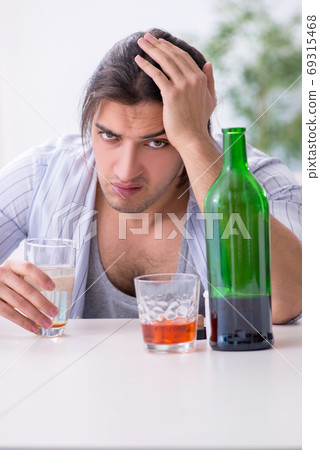 Young male alcoholic drinking whiskey at home 69315468