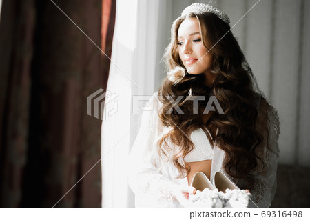 Beautiful luxury bride in elegant white dress holds wedding shoes in the hands 69316498