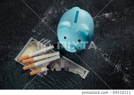 Blue piggy bank and cigarettes on dark table. Expensive habit 69318111