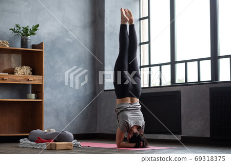 Woman practicing yoga near window in headstand exercise, salamba sirsasana 69318375