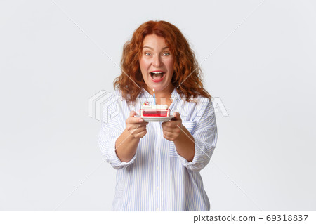 Celebration, holidays and emotions concept. Excited and upbeat redhead middle-aged woman enjoying party in her honor, holding birthday cake with lit candle, making b-day wish 69318837